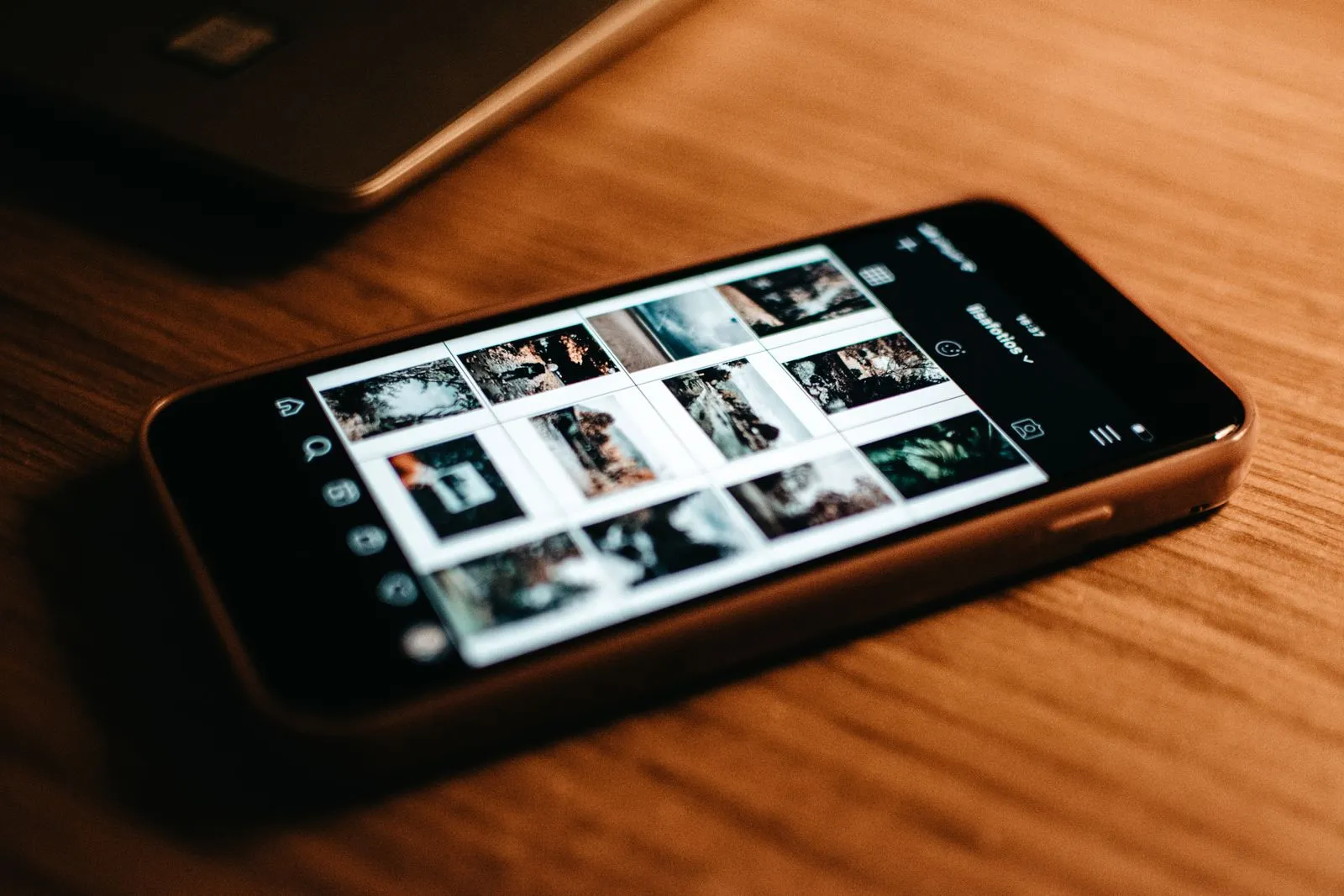 A phone lying on a wooden desk, its screen filled with a grid of thumbnails